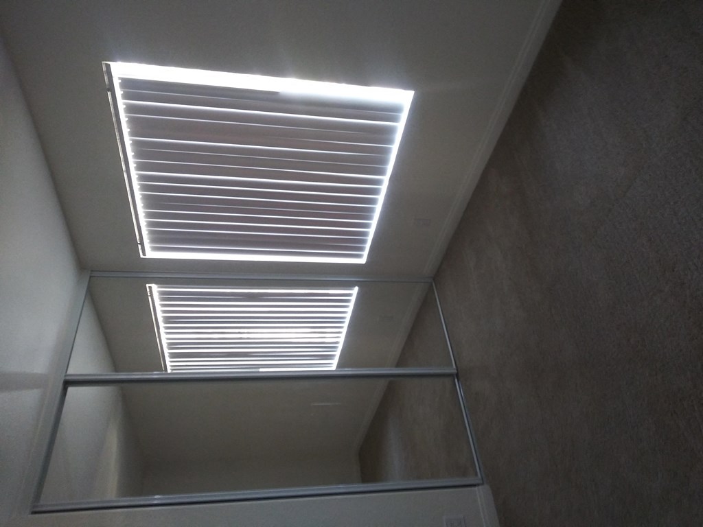 Carpeted bedroom with mirrored closet doors and large window with vertical blinds at La Costa Seashore Apartments in Carlsbad, CA