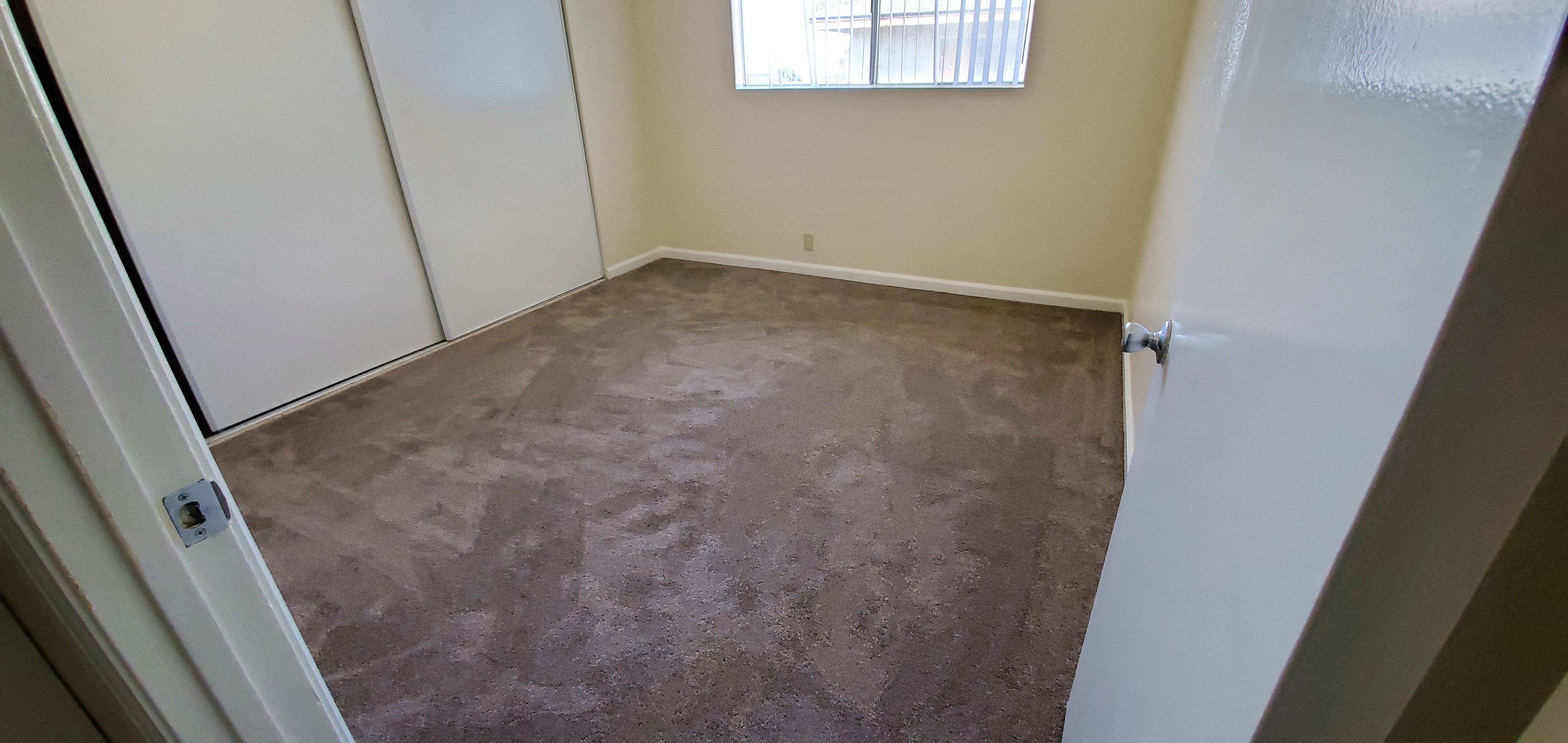 Carpeted bedroom with large closets and window at Zenith Place Apartments in Chula Vista, California.