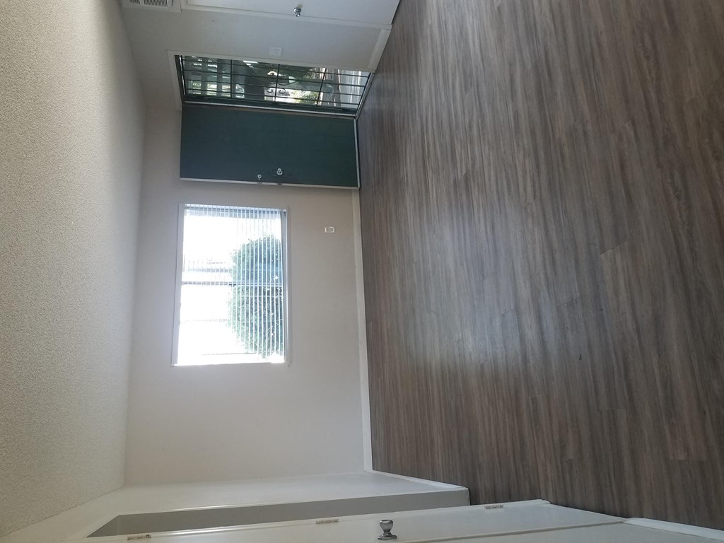 Living room with hardwood flooring, large window and front door with security screened door at Tulip Street Apartments in Escondido, California.