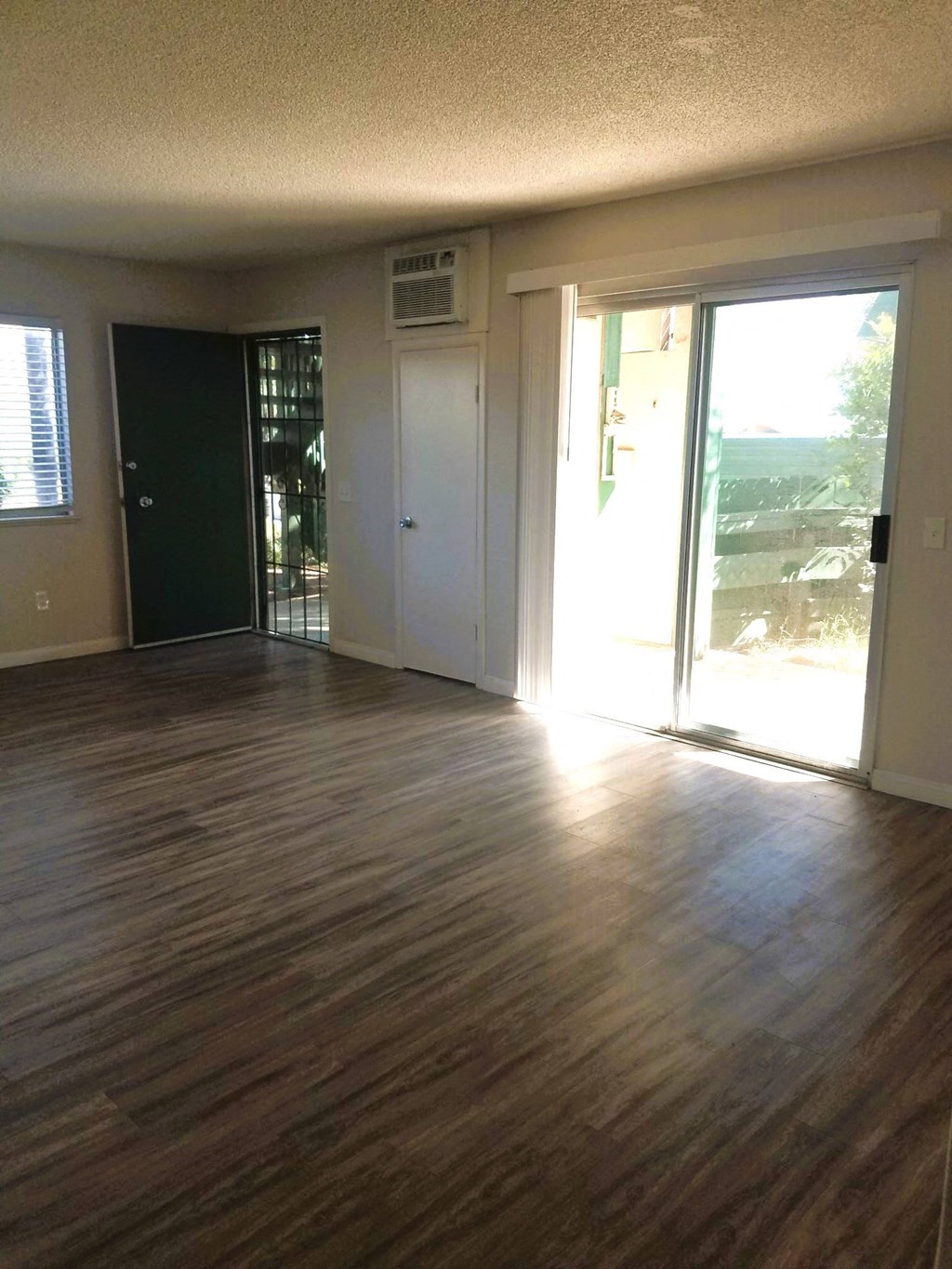 Living room with hardwood flooring and sliding glass doors to patio in unit at Tulip Street Apartments in Escondido, California.