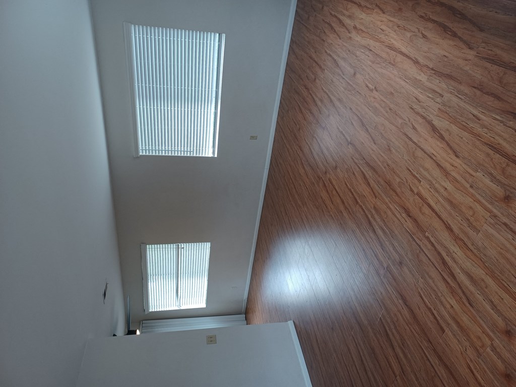 Living room with hardwood flooring and large windows for lots of natural light in apartment home at Juniper Street Apartments in Escondido, California.