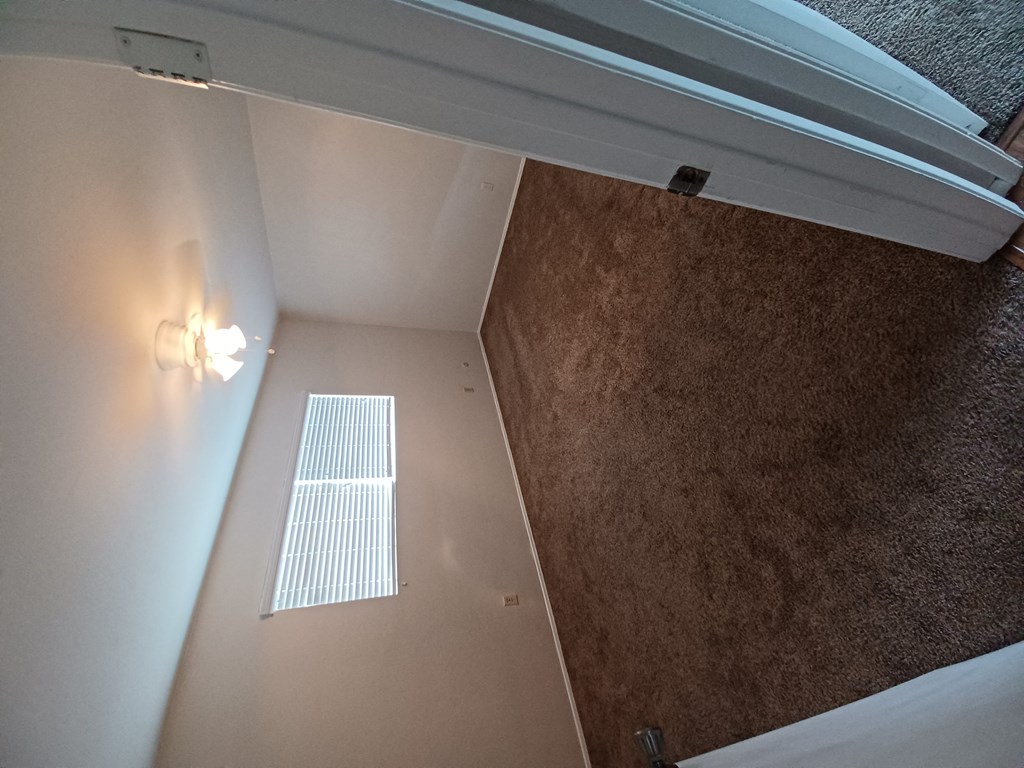 Carpeted bedroom with large double window and ceiling fan at Juniper Street Apartments in Escondido, California.