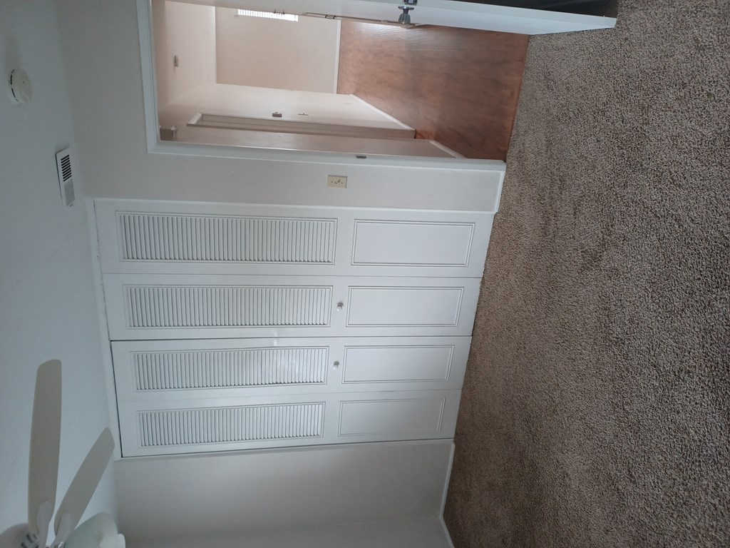Carpeted bedroom with ceiling fan and large closets at Juniper Street Apartments in Escondido, California.