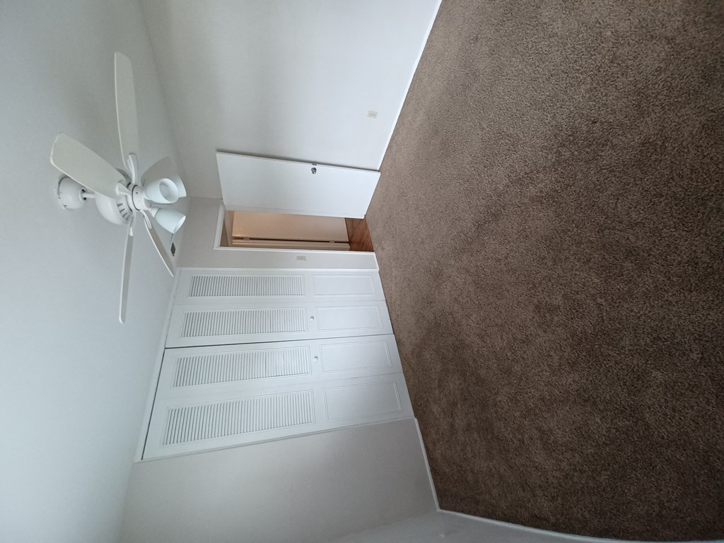 Carpeted bedroom with large closets and ceiling fan at Juniper Street Apartments in Escondido, California.