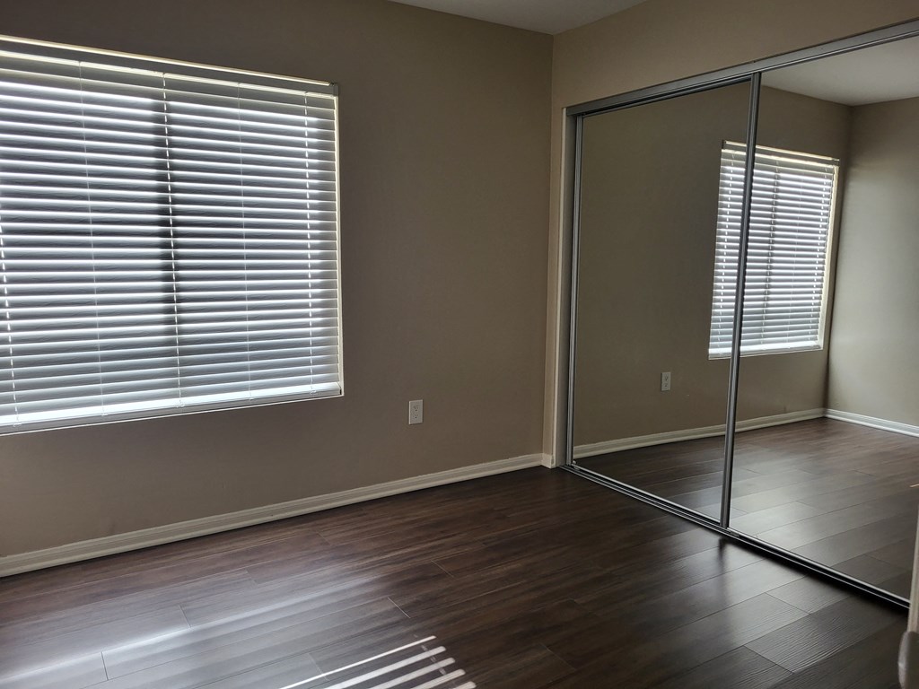 Bedroom with plank style flooring, large window and large closet with sliding mirror doors at The Cove at Bear Valley in Escondido, California.