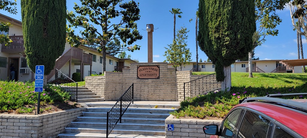 Parking lot steps to apartment walkways with mature landscaping and lots of grassy open space at Plaza Verde Apartments in Escondido, California.
