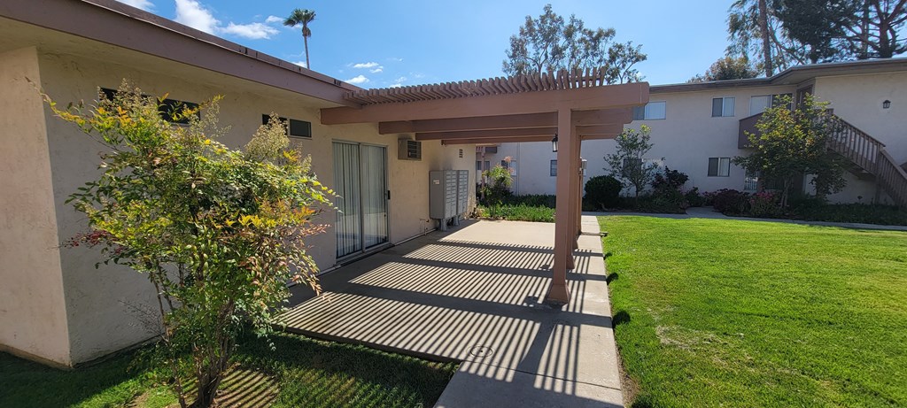 Patio with pergola and mailboxes in grassy courtyard at Plaza Verde Apartments in Escondido, California.