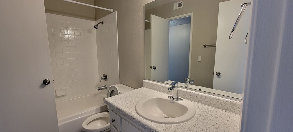 Shared bathroom with white fixtures and vanity cabinets at La Mesa Village Apartments in La Mesa, California.