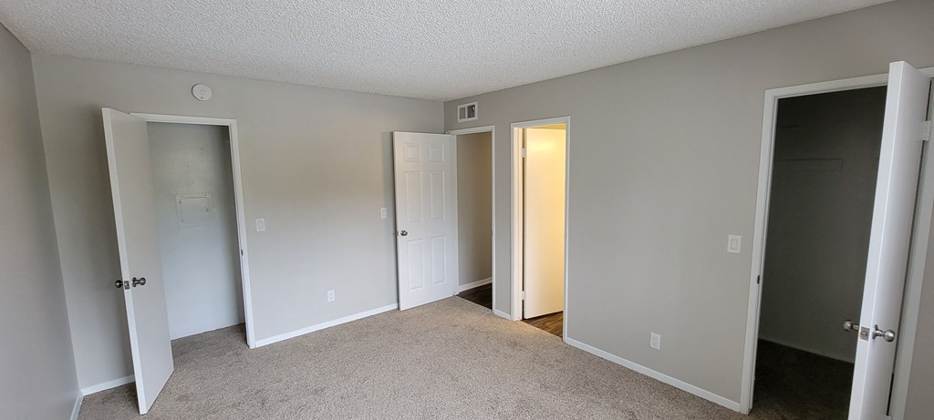 Carpeted master bedroom with two walk-in closets and shared bathroom at La Mesa Village Apartments in La Mesa, California.
