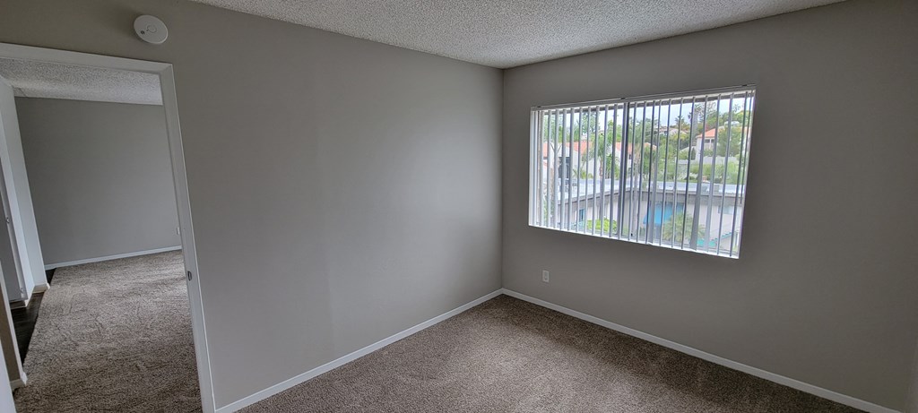 Carpeted bedroom with large window at La Mesa Village Apartments in La Mesa, California.