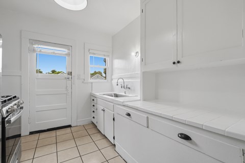 A white kitchen with a stove, sink, and cabinets.