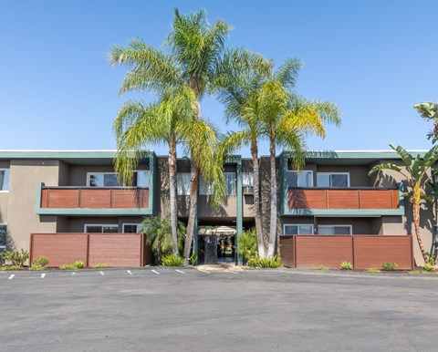 A building with a parking lot in front of it and palm trees in the background.