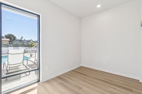 A room with a wooden floor and white walls, with a glass door leading to a pool area.