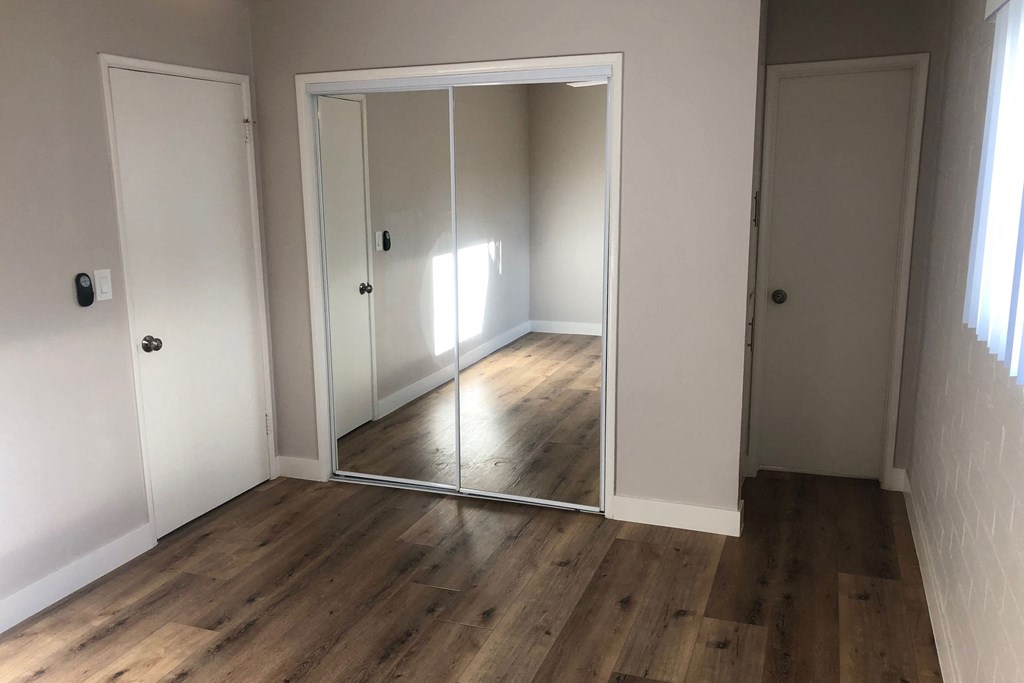 Bedroom with wood plank style vinyl flooring and mirrored closet doors at 5747 Lauretta Street Apartments in San Diego, California.