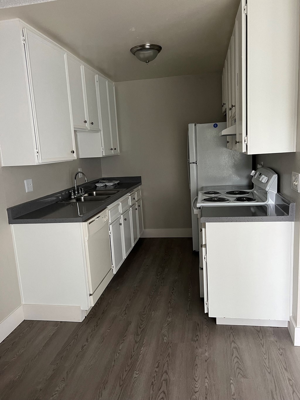 Kitchen with plank style flooring, spacious whit cabinets, dishwasher, refrigerator, and electric stove/oven at IKARIA Apartments in Santee, California.