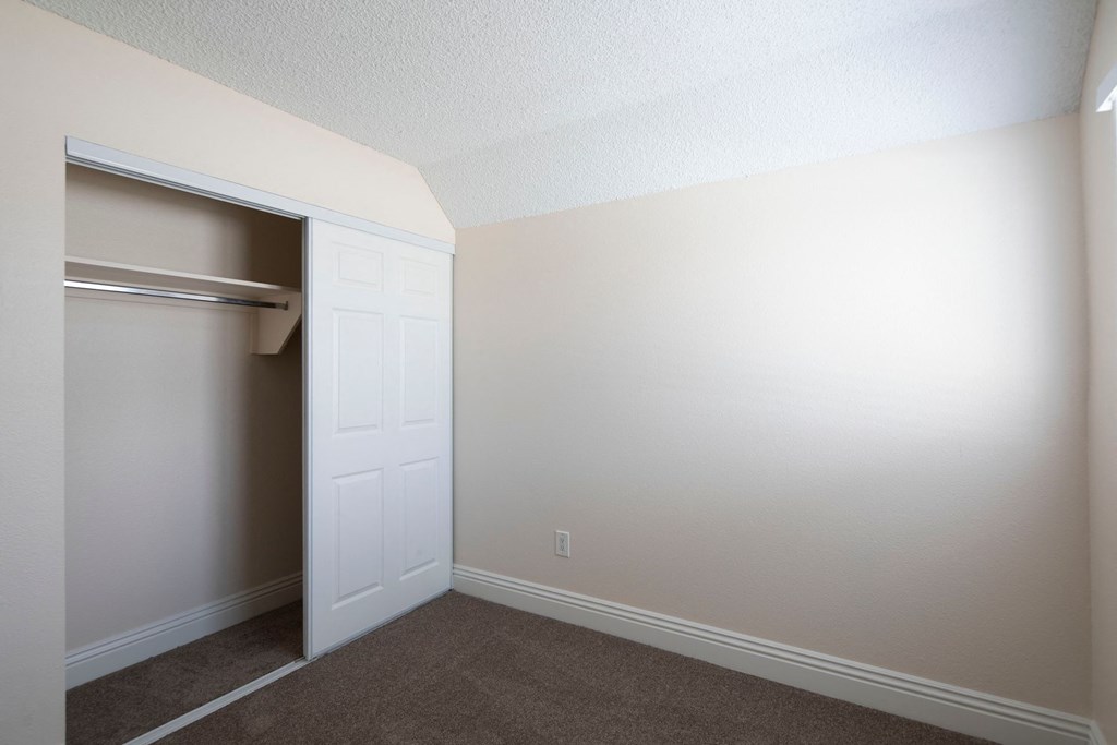 Carpeted bedroom with large closet and window at the Atrium Apartments in San Diego, California.