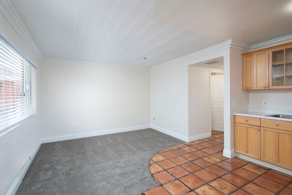 Open kitchen with Saltillo tile flooring and front room with berber carpeting and large window at the Atrium Apartments in San Diego, California.