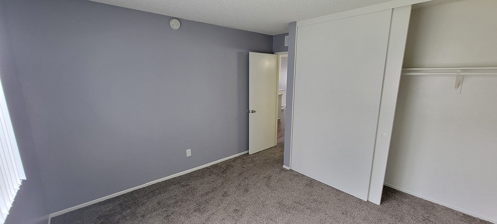 Carpeted bedroom with large window and closet at Grand Oaks Apartments in Lake Elsinore, California.