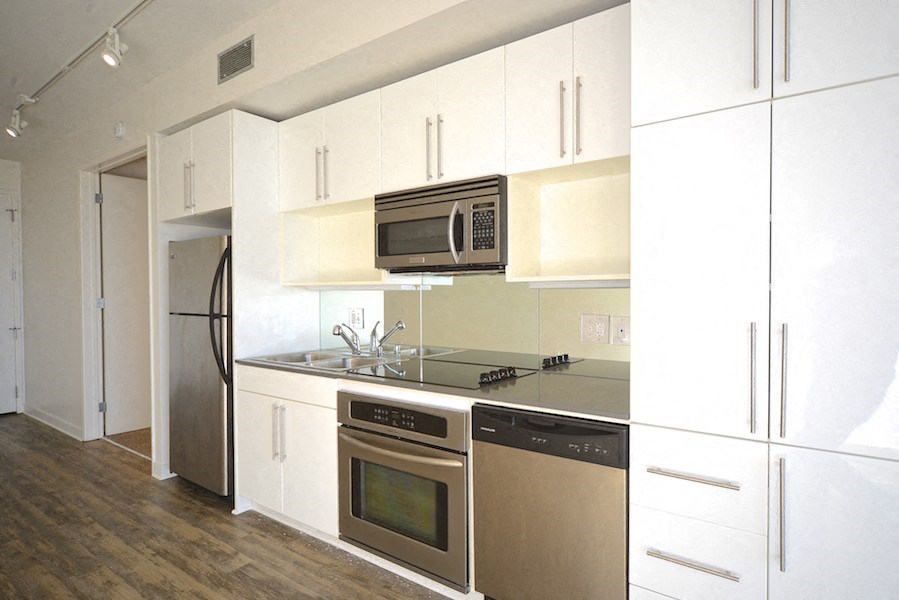Kitchen area with spacious white cabinets, electronic stove/oven, microwave, dishwasher, and refridgerator at 12th Street Lofts in National City, California.