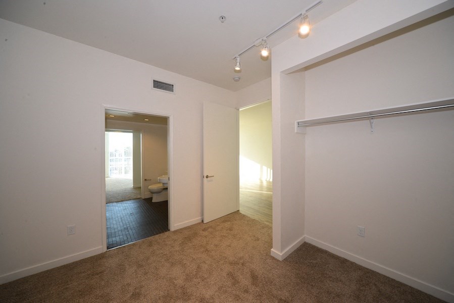 Carpeted bedroom with spacious closets and shared bathroom at 12th Street Lofts in National City, California.