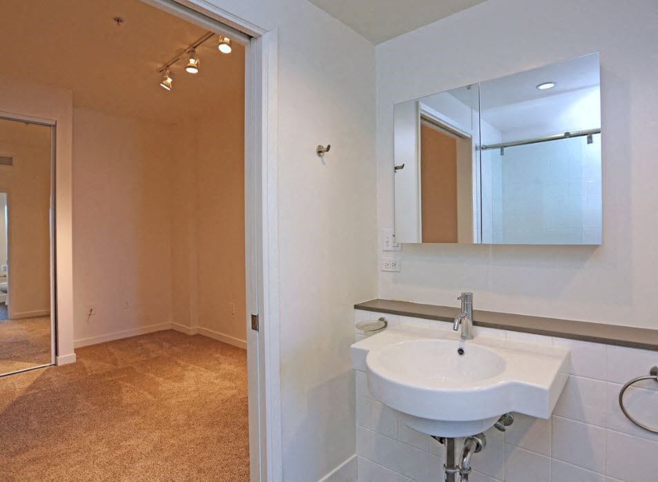 Bathroom and carpeted bedroom with large mirrored door closets at 12th Street Lofts in National City, California.