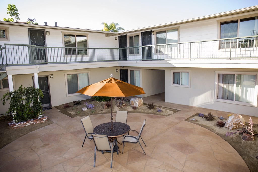 Patio with umbrella shaded table and chairs at Harbor Villa Apartments in San Diego, California.