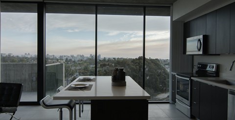 A modern kitchen with a table and chairs in front of large windows overlooking a cityscape.