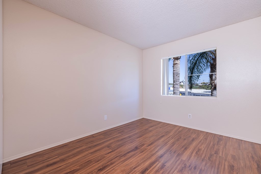 Empty room with wooden floor and a window showing a view of a street.