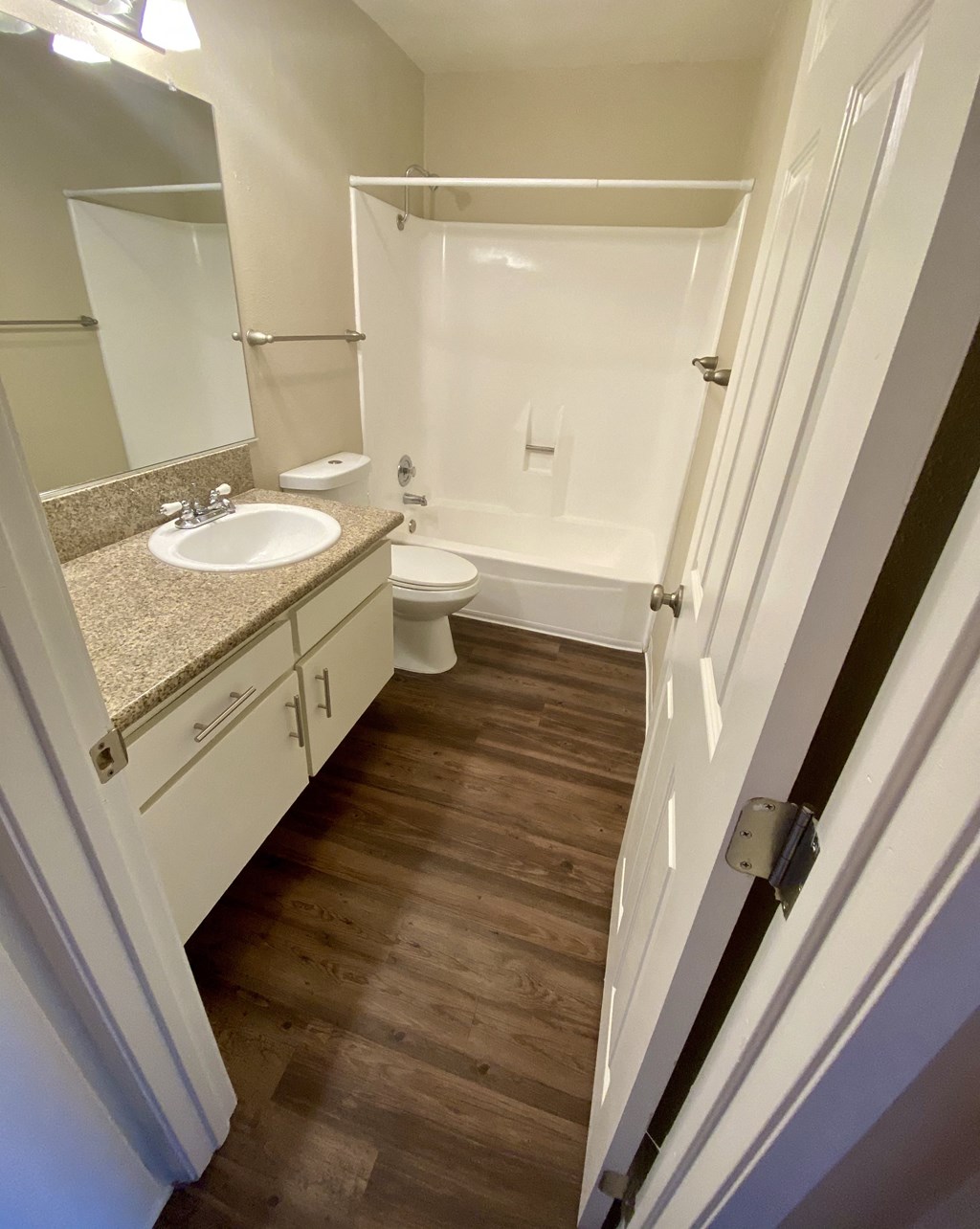 Bathroom with plank style flooring, white vanity cabinets and white fixtures in unit at Villa Pacific Apartments in Oceanside, California.