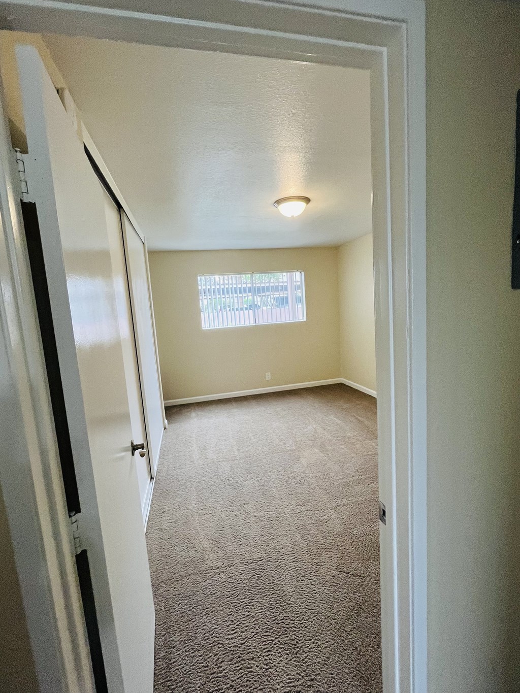 Carpeted bedroom with large window and closet at Plaza Verde Apartments in Escondido, California.
