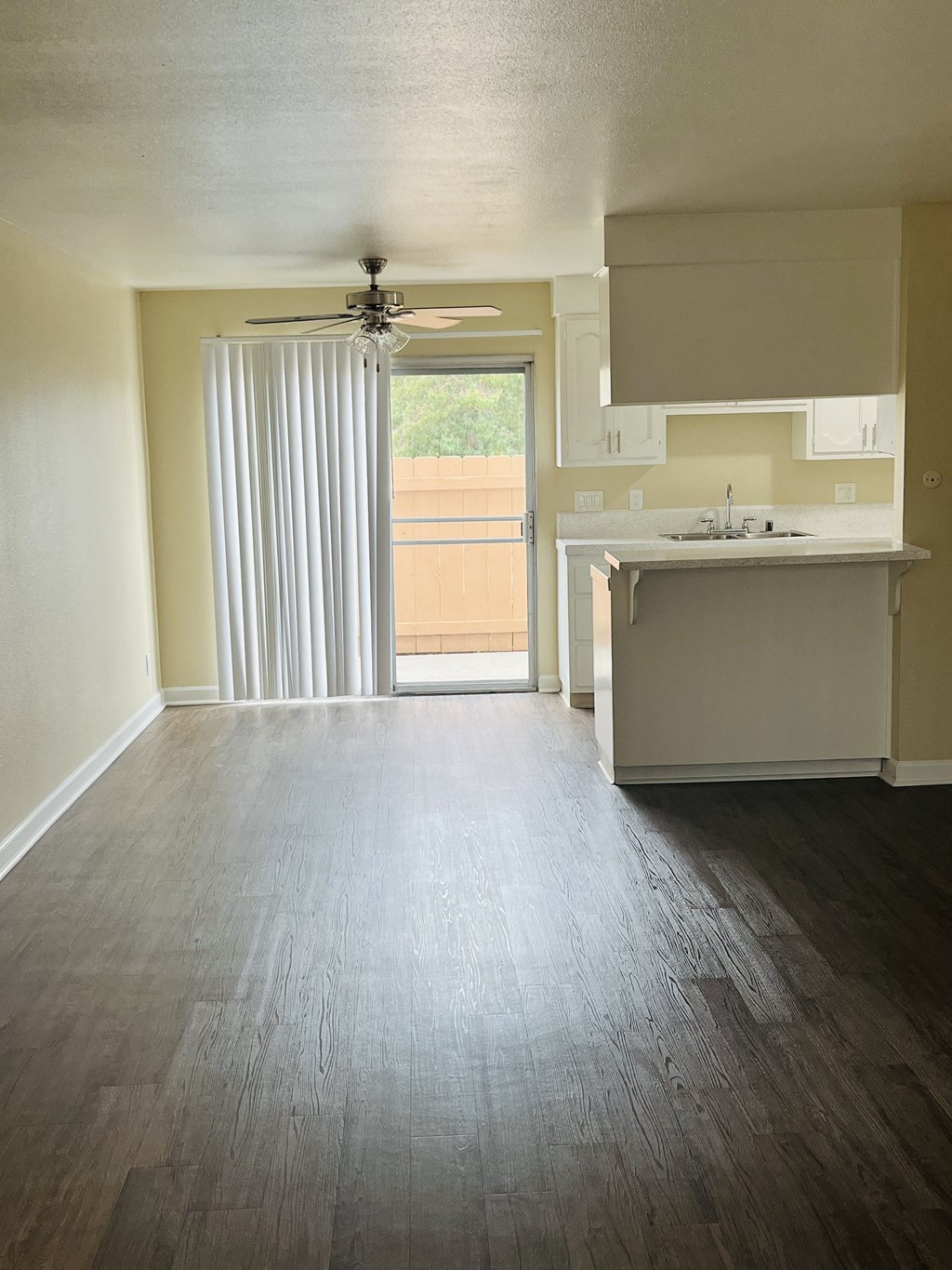Kitchen, dining area with ceiling fan and living room with sliding glass doors to patio at Plaza Verde Apartments in Escondido, California.