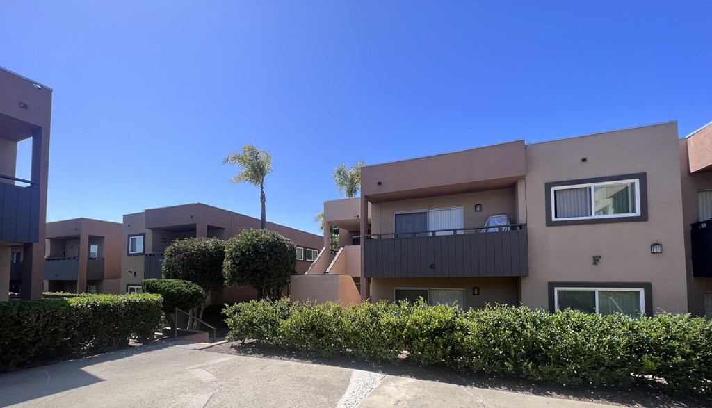 Private patios and balconies amongst manicured bushes and trees at Villa Pacific Apartments in Oceanside, California.