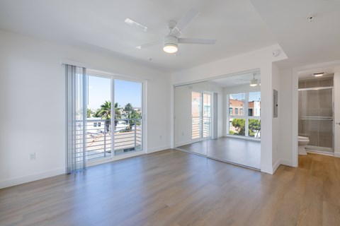 A spacious room with a ceiling fan and sliding glass doors leading to a balcony.