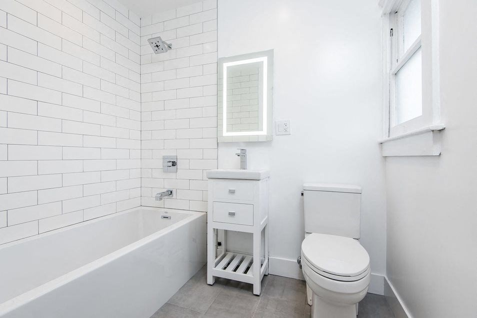 Bright bathroom with white modern fixtures and wood plank style flooring at 4141 Normal Avenue apartment homes in Los Angeles, California.