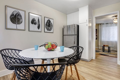 a dining area with a round table with four chairs and a stainless steel refrigerator in the background