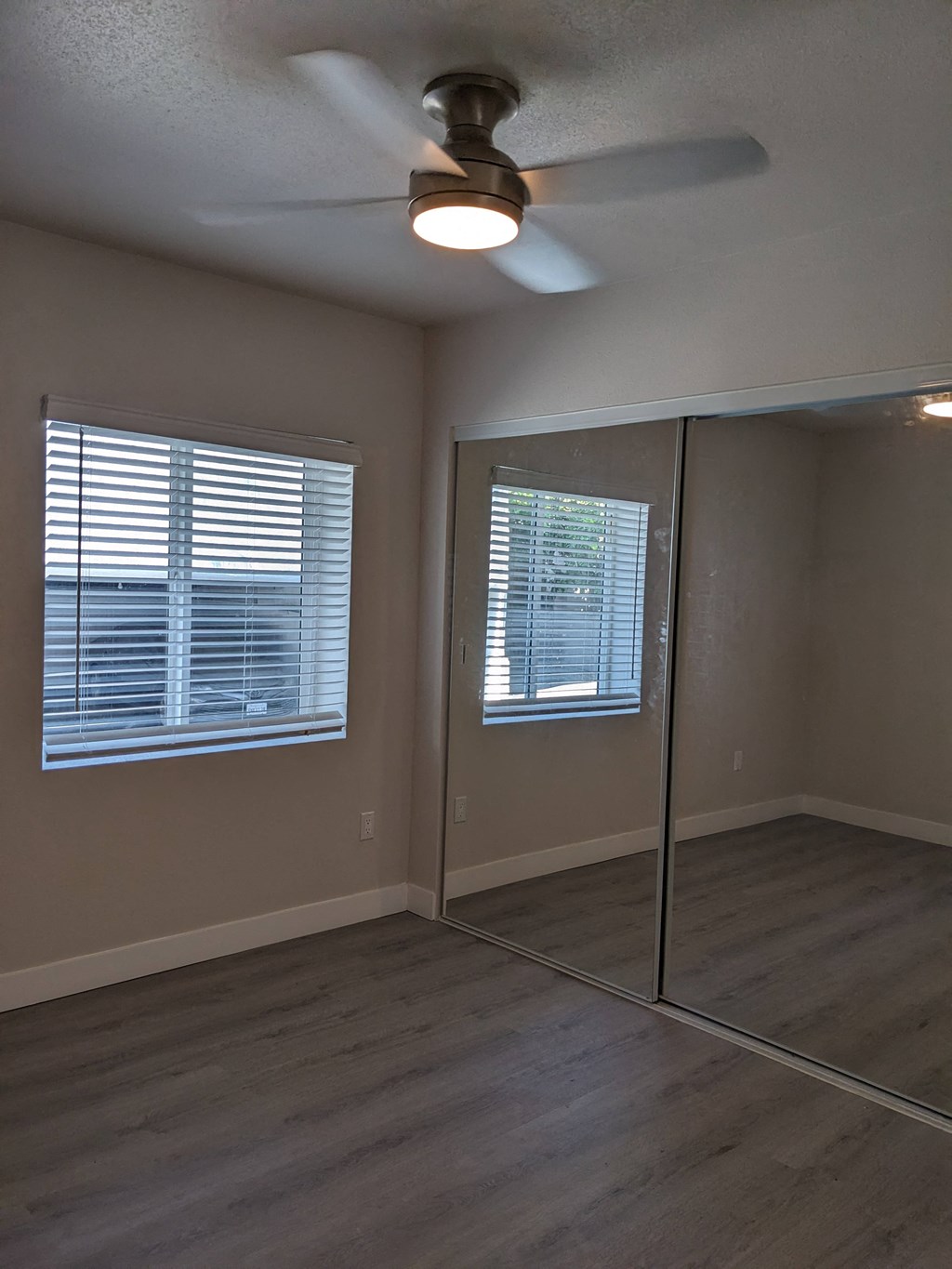 Bedroom with large window, mirrored closet doors, ceiling fan, and wood plank style flooring at The Hardison in Pasadena, California.