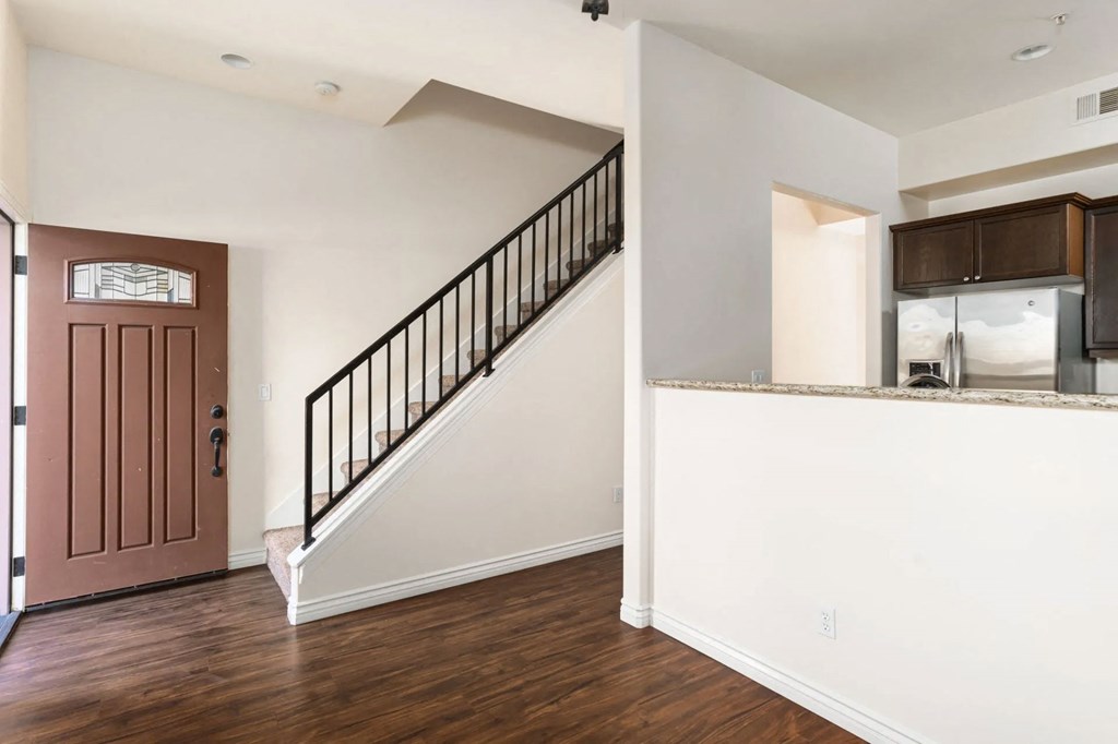 Front entrance with wood style laminate flooring and view of open kitchen with dark wood cabinetry at The Nines Townhomes in Escondido, California.