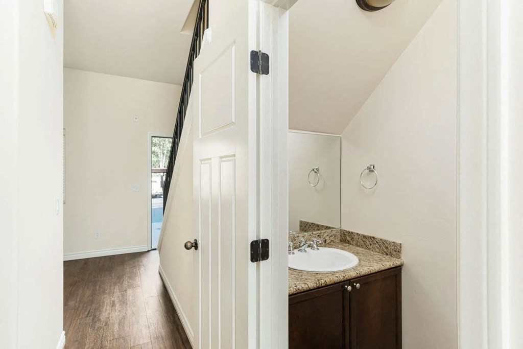 Half bathroom downstairs with dark wood vanity and granite slab top and upgraded fixtures in apartment at The Nines Townhomes in Escondido, California.