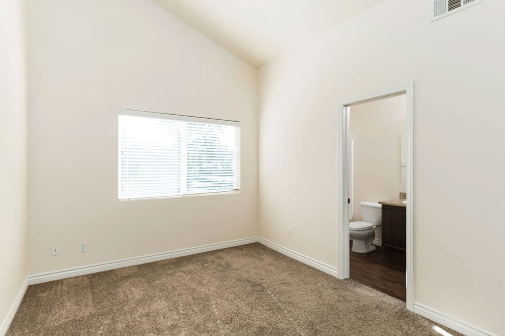 Carpeted bedroom with cathedral ceiling, larage window and bathroom at The Nines Townhomes in Escondido, California.
