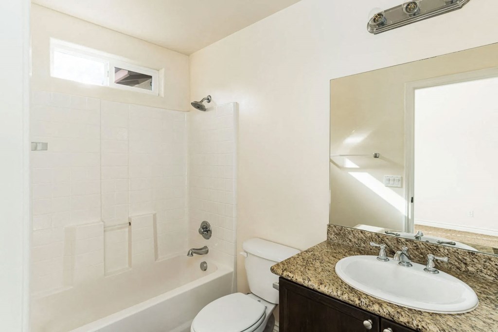 Bathroom with granite slab vanity counter top, white fixtures, upgraded faucets, and privace window for natural light at The Nines Townhomes in Escondido, California.