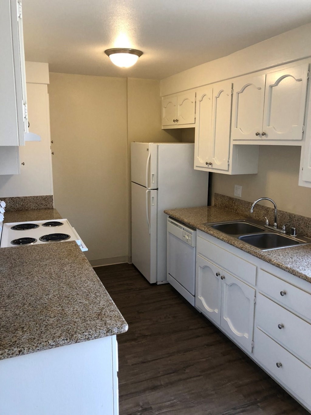 Kitchen with spacious white cabinets, plank style flooring, refrigerator, dishwasher, microwave, and electric stove at Plaza Verde Apartments in Escondido, California.