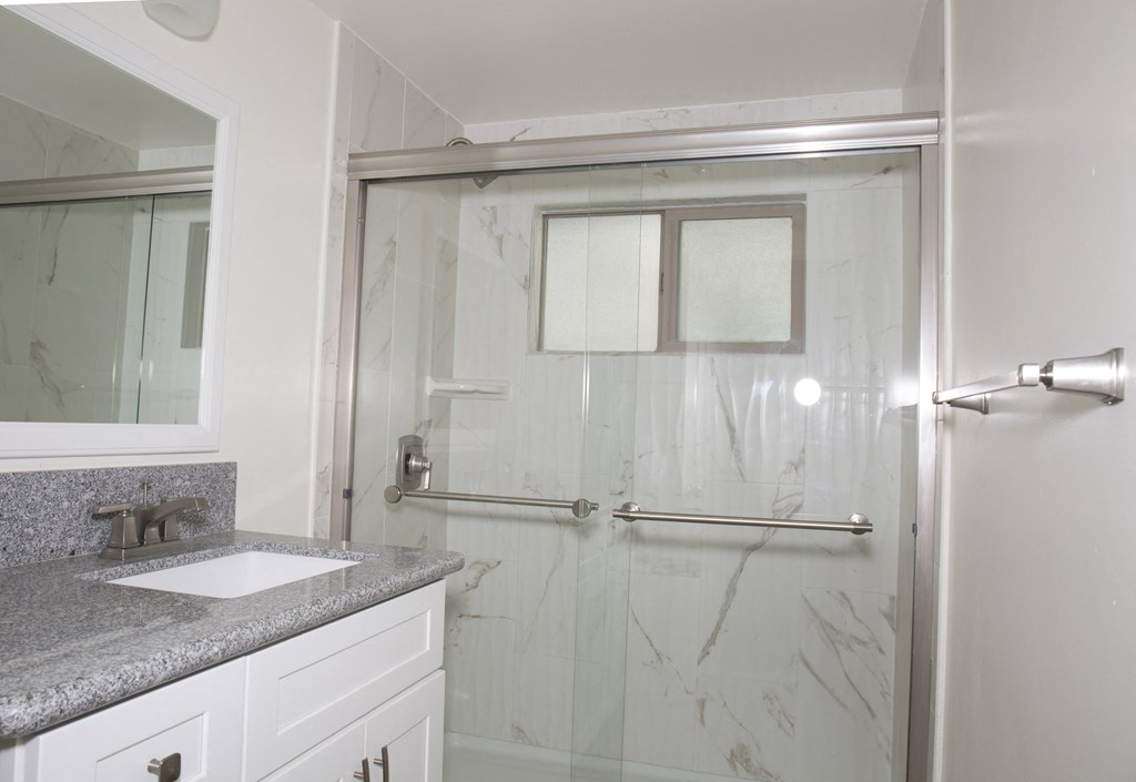 Bathroom with walk-in shower and white cabinets at Harbor Villa Apartments in San Diego, California.