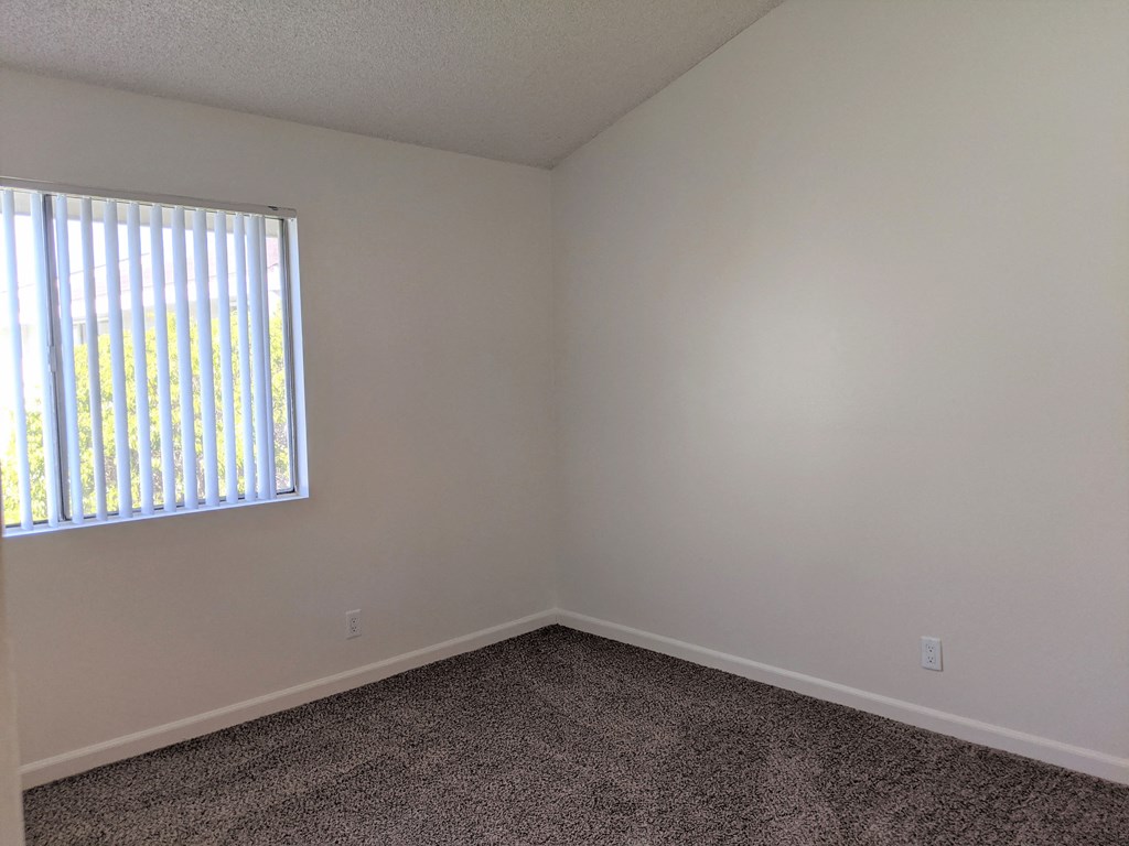 Carpeted bedroom with nice natural lighting and vertical blinds in apartment unit at the Steckel Apartments in Santa Paula, California.