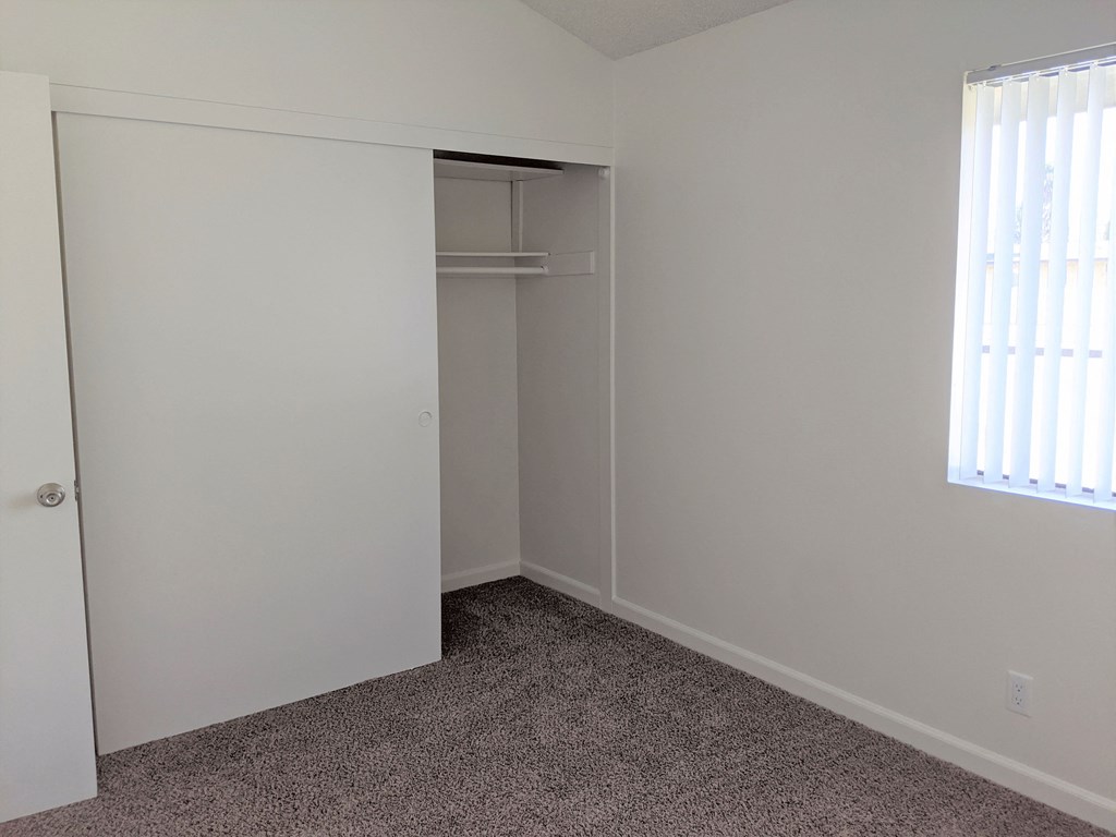 Carpeted bedroom with large closet and large window at the Steckel Apartments in Santa Paula, California.