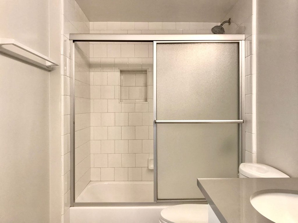 White bathroom with white fixtures and sliding shower door in apartment at Summer House Apartments in Ventura, California.