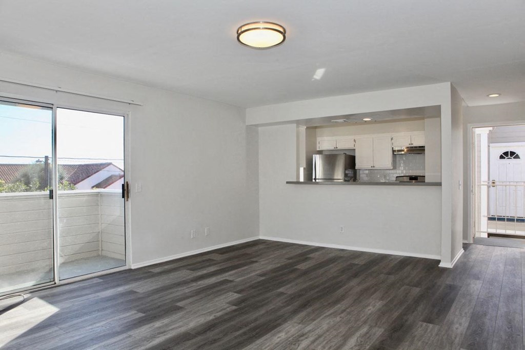 Living room with view of kitchen and patio in unit at Summer House Apartments in Ventura, California.