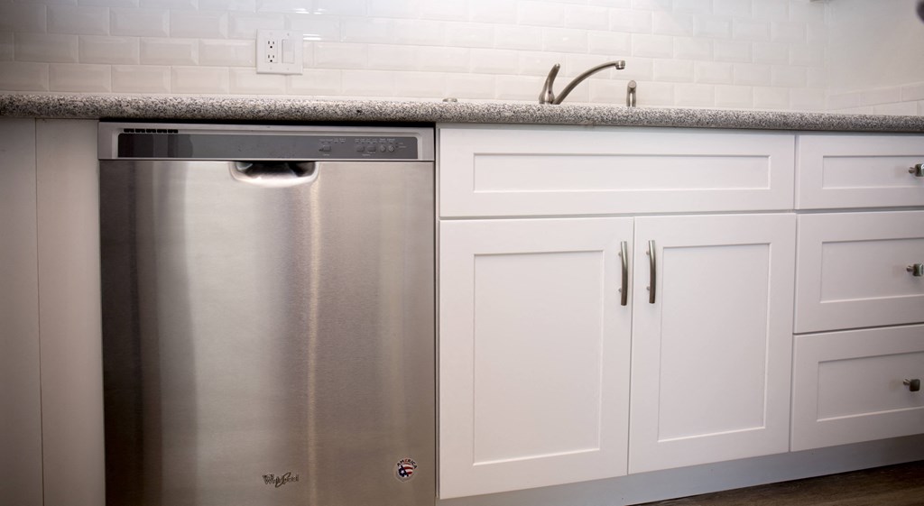 Kitchen with dishwasher and spacious white cabinets at Harbor Villa Apartments in San Diego, California.