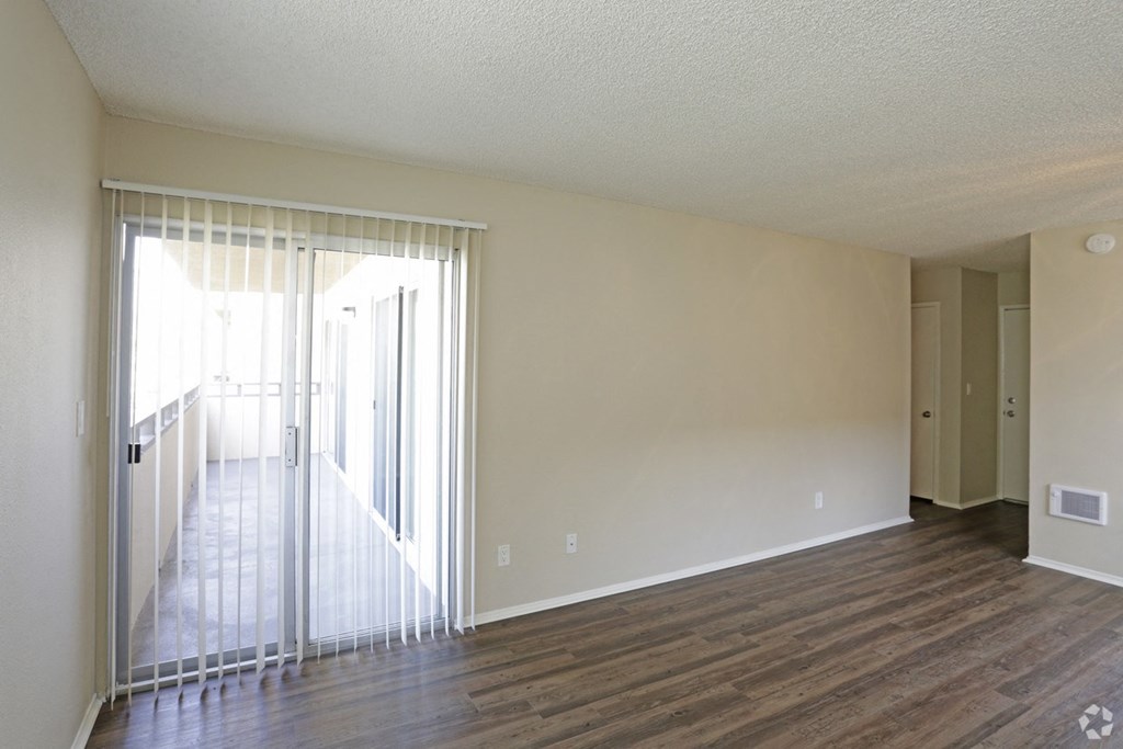 Living room with plank style flooring and sliding glass doors to private porch at Villa Pacific Apartments in Oceanside, California.