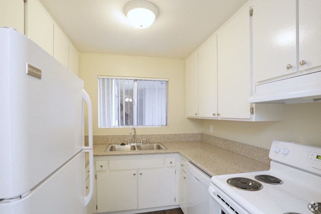 Kitchen with white appliances including refrigerator, dishwasher, and electric range at Villa Pacific Apartments in Oceanside, California.