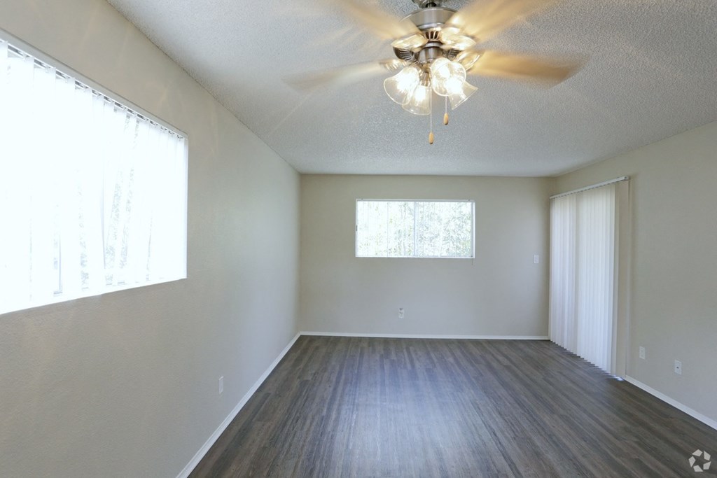 Dining araa with ceiling fan and living room with plank style flooring and lots of windows for natural light at Villa Pacific Apartments in Oceanside, California.